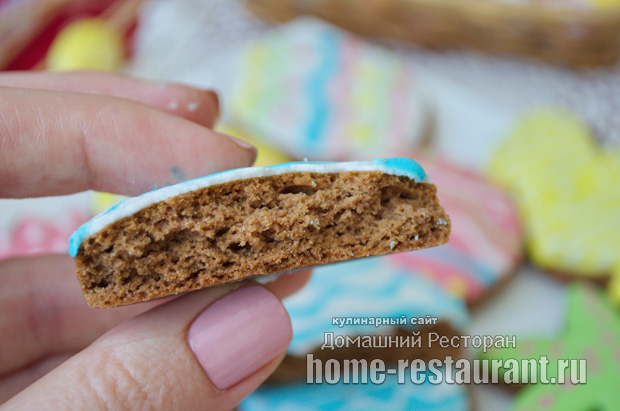 Крупный план готового имбирного пряника на пасху, украшенного белой глазурью, и кусочка пряника в разрезе, демонстрирующего пористую и мягкую текстуру теста. 